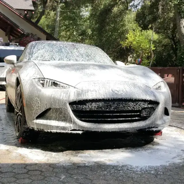 A Mazda MX-5 covered in snow foam during a hand wash on a paver driveway in Westlake Village, CA