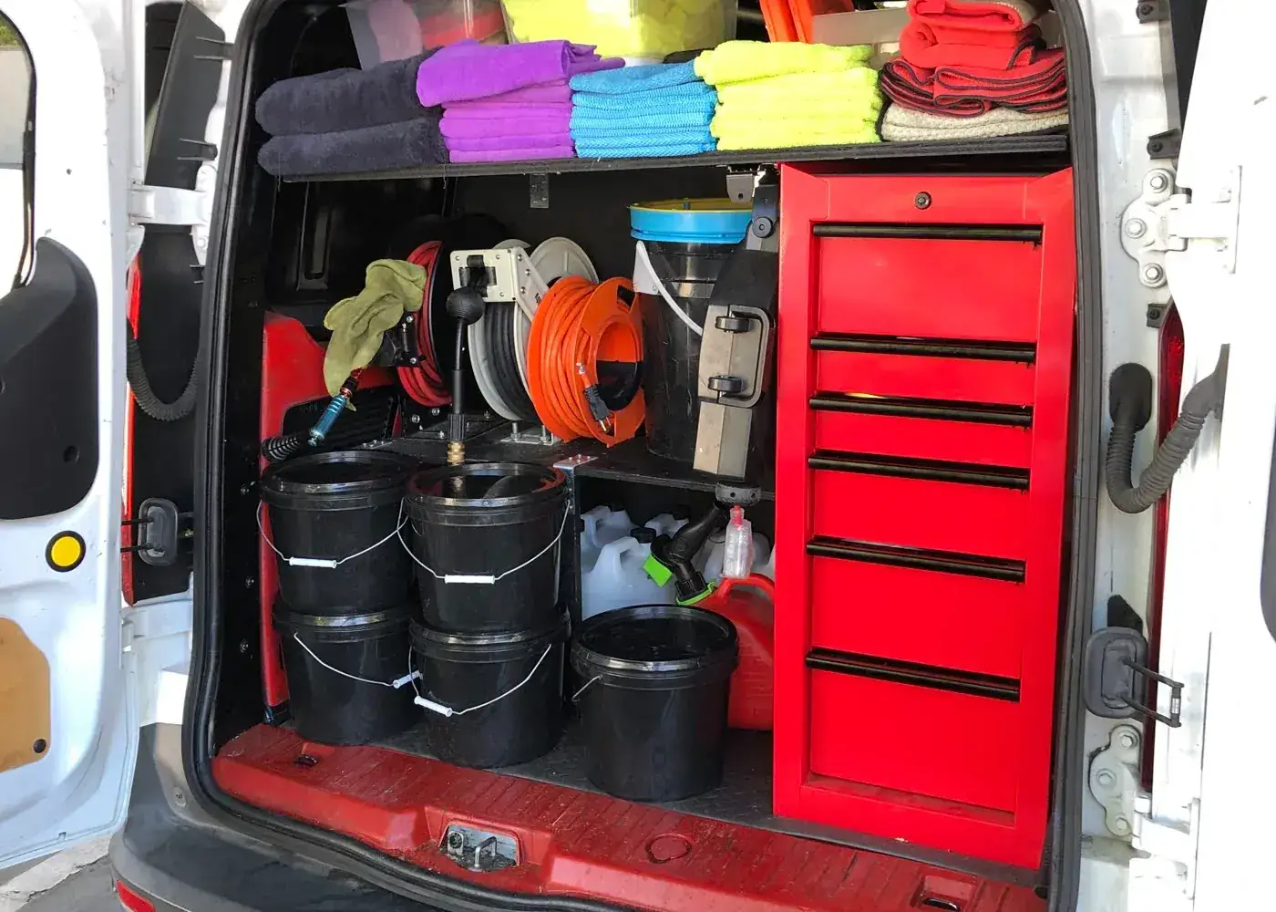 The TailorMade Mobile Auto Detailing van open, showing folded microfibre towels, hose reels, buckets and the tool chest